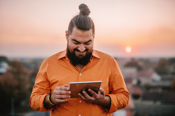 Young urban man standing at the top of the building holding tablet.