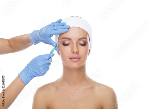 Fotomural Beautiful face of the young woman and the medical scalpel in doctor's hands isolated on white