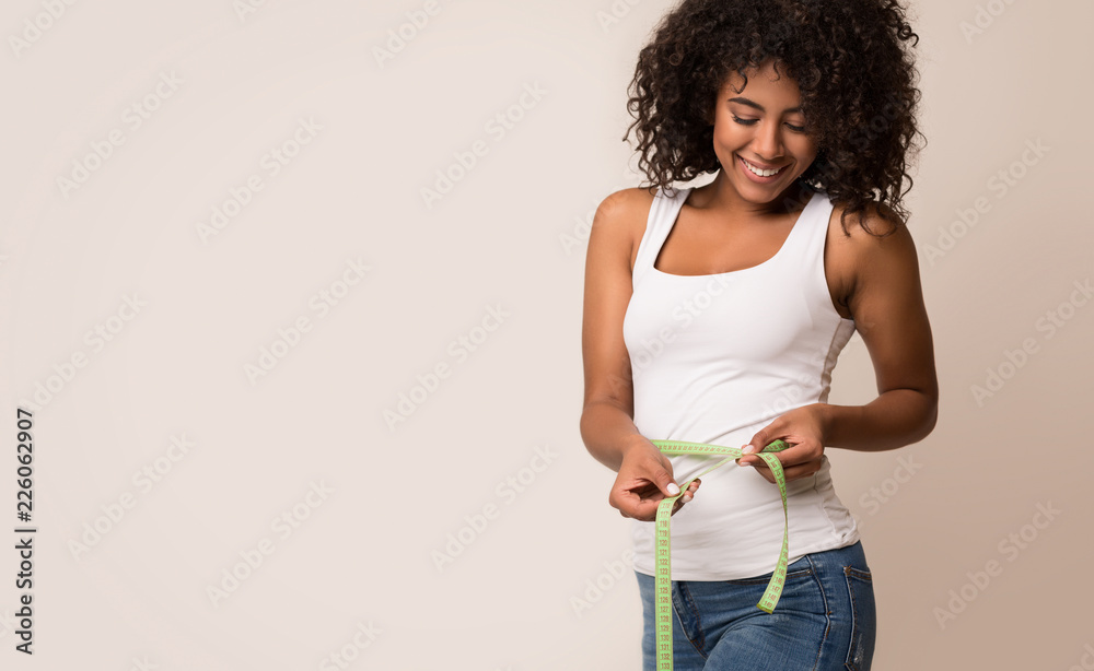 African-american woman measuring waist and looking on tape - obrazy, fototapety, plakaty 