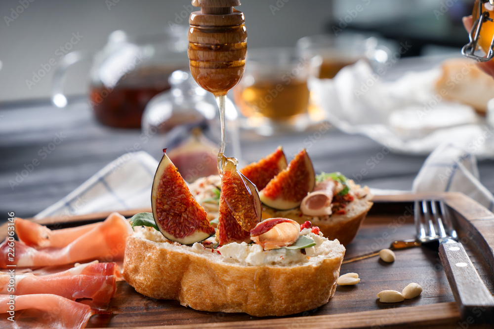 Sweet honey dripping from dipper onto sandwich with ripe fig