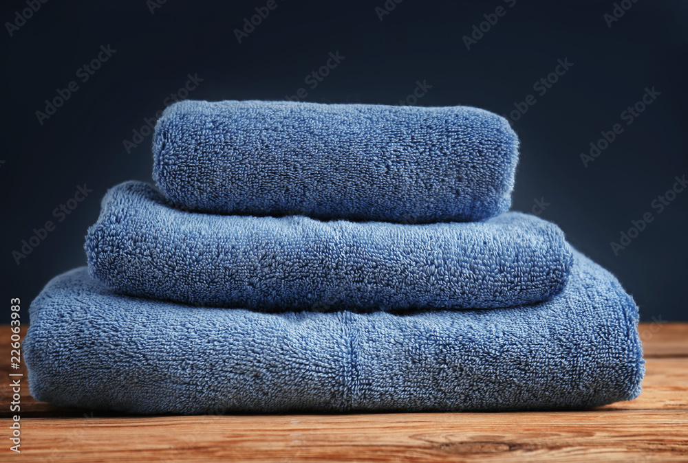 Stack of clean soft towels on wooden table against color background