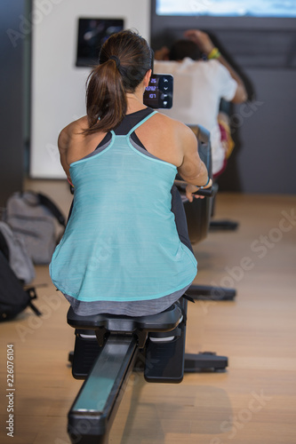 Fotografie, Obraz Athletic Girl Exercising on Rowing Machine at Gym: Fitness Equipment