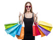 Happy brunette woman wears black dress and sunglasses holding colorful shopping bags and shows thumb up signs, women shopaholic sale concept