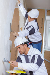 two builders in hardhats and overalls with spatula repairing room