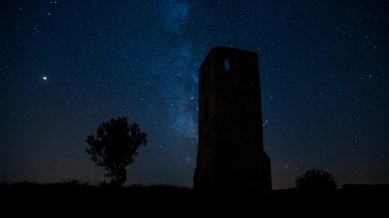 Wall Mural - the milky way moving across the night sky and an ancient castle tower lit by the moonrise in a clear
