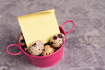 Sticker - One pink metal rural basin with handles full of spotted fresh quail eggs and yellow curved blank paper sticker on old broken worn gray cement floor