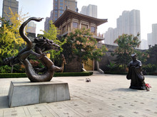 Statue Of A Man And Dragon In Front Of Stylized City Wall With Blooming Trees In Spring. Qujiang District, Xian City, Shaanxi Province, China. Modern Chinese City.