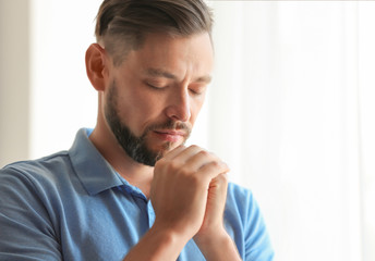 Man with hands clasped together for prayer on light background. Space for text