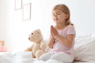 Little girl praying in bed at home. Space for text