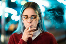 Millennial Pretty Girl With Unusual Dyed Hairstyle Smoking Cigarette In Amusement Park At Night. Blue Hair, Golden Sequins As Freckles,nose Piercing. Mysterious Hipster.