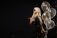 Brightfull Expressions Of Happy Emotions Of  Amazing Blonde Girl Celebrating Party On Black Background. Luxury Black Dresses, Smiling, A Glass Of Champagne, Golden Tinsels,  Balloons, Long Curly Hair