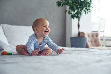 cute baby boy playing with knitted toy on bed at home