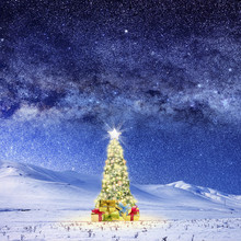 Conceptual Image Of Decorated Christmas Tree On Snow Covered Landscape Over Night Sky With Stars And Galaxies.