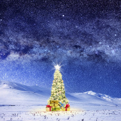 Wall Mural - Conceptual image of Decorated Christmas tree on snow covered landscape over night sky with stars and galaxies.