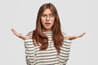 © wayhome.studio  - Questioned indignant pleasant looking brunette woman speads hands in hesitant gesture, wears striped casual sweater, looses something, forgets about some details, has frustrated facial expression