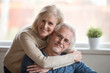 © fizkes - Smiling caring middle aged wife embracing senior husband at home, happy old woman hugging loving mature man looking at camera, retired elderly family married couple dating bonding headshot portrait