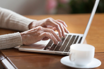 Mature female hands typing text on keyboard, senior elderly business woman working on laptop, old or middle aged lady using computer concept writing emails, communicating online, close up view