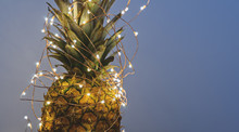 Close Up View Of Pineapple With Christmas Light Garland With Copy Space, Greeting Card Concept On Gray Background Banner