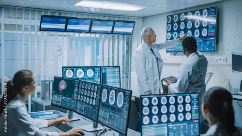 Team of Professional Medical Scientists Work in the Brain Research Laboratory. Neurologists / Neuroscientists Surrounded by Monitors Showing CT, MRI Scans Having Discussion and Working on PС