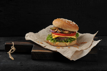 Cheeseburger on craft paper. Dried onions are scattered around the cheeseburger. Black background. Close-up. 