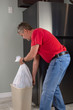 Man in a red tee shirt doing house chores emptying the full trash bag bin container in the kitchen so he can take it to the garbage cans outside.