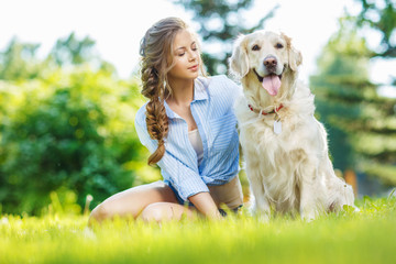 Young woman sitting on the grass with golden retriever dog in the summer park