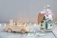 Glass Jar With Money And Paper Heart Next To Wooden Toy Car On Wooden Background