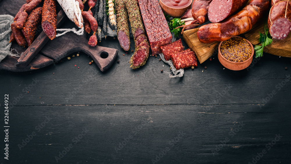 Assortment of salami and snacks. Sausage Fouet, sausages, salami, paperoni. On a black wooden background. Top view. Free space for your text. - obrazy, fototapety, plakaty 
