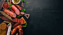 Assortment Of Salami And Snacks. Sausage Fouet, Sausages, Salami, Paperoni. On A Black Wooden Background. Top View. Free Space For Your Text.
