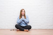 © Krakenimages.com - Young adult woman sitting on the floor in autumn over white brick wall praying with hands together asking for forgiveness smiling confident.