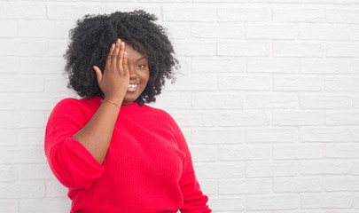 Poster - Young african american plus size woman over white brick wall covering one eye with hand with confident smile on face and surprise emotion.