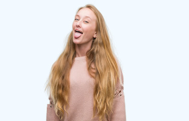 Canvas Print - Blonde teenager woman wearing pink sweater sticking tongue out happy with funny expression. Emotion concept.