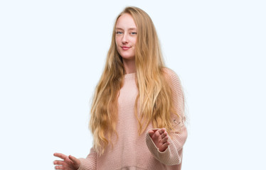 Wall Mural - Blonde teenager woman wearing pink sweater disgusted expression, displeased and fearful doing disgust face because aversion reaction. With hands raised. Annoying concept.