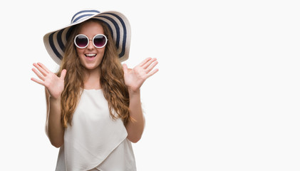 Wall Mural - Young blonde woman wearing sunglasses and summer hat very happy and excited, winner expression celebrating victory screaming with big smile and raised hands