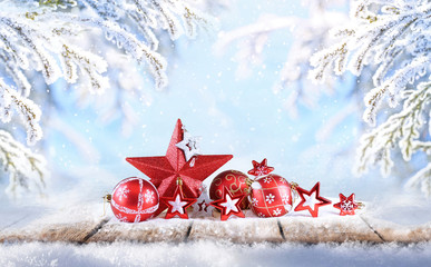 Poster - Festive Christmas composition of balls and red stars on wooden platform in forest outdoors framed by snow-covered fir branches with copy of space.