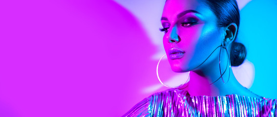 Wall Mural - Fashion model brunette woman in colorful bright neon lights posing in studio. Beautiful sexy girl, trendy glowing makeup, metallic silver lips