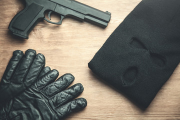 Pistol, balaclava and gloves on wooden background. Criminal concept