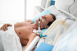 Stable condition. Side view portrait of patient on mechanical ventilator lying in bed under white sheets