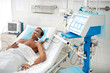 Portrait of unconscious middle aged man on mechanical ventilator lying in hospital bed under white sheets