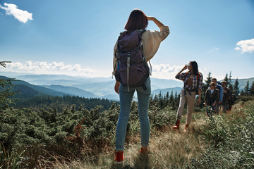 Wall Mural - Rear view of a slim female tourist standing on the mountain hill while waiting for her friends