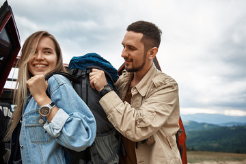 Wall Mural - Delighted smiling young woman wearing a backpack with her boyfriend while resting outdoors