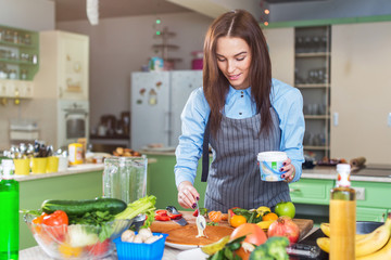 Happy young woman making cake smearing a layer with cream standing in kitchen