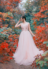 Wall Mural - cute girl with dark hair and a neat haircut dressed in a long pink peach tender luxurious dress stands in the forest with green and red leaves. Autumn landscape. creative colors. art photo processing