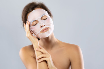 Wall Mural - woman with a sheet moisturizing mask on her face isolated on gray background