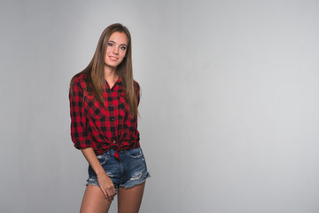 Wall Mural - Young beautiful woman teenager in a red checked shirt and torn denim shorts