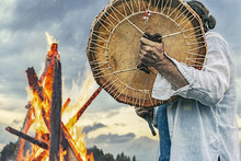 Shaman Plays Drums Near The Big Fire On The Sky Background