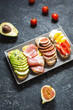 A set of avocado sandwiches, cherry tomatoes and eggs, figs, prochutto on a stone background.