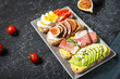 A set of avocado sandwiches, cherry tomatoes and eggs, figs, prochutto on a stone background