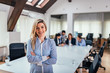© bnenin - Beautiful female leader standing and looking at camera. Startup business people group working in the background.