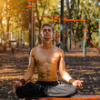 young male athlete on a street court sitting in a lotus yoga pose outdoors